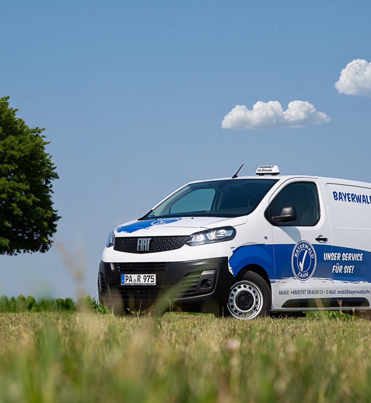 Mobiles Zahnarztfahrzeug von Bayerwaldzahn steht auf einer Wiese unter blauem Himmel.